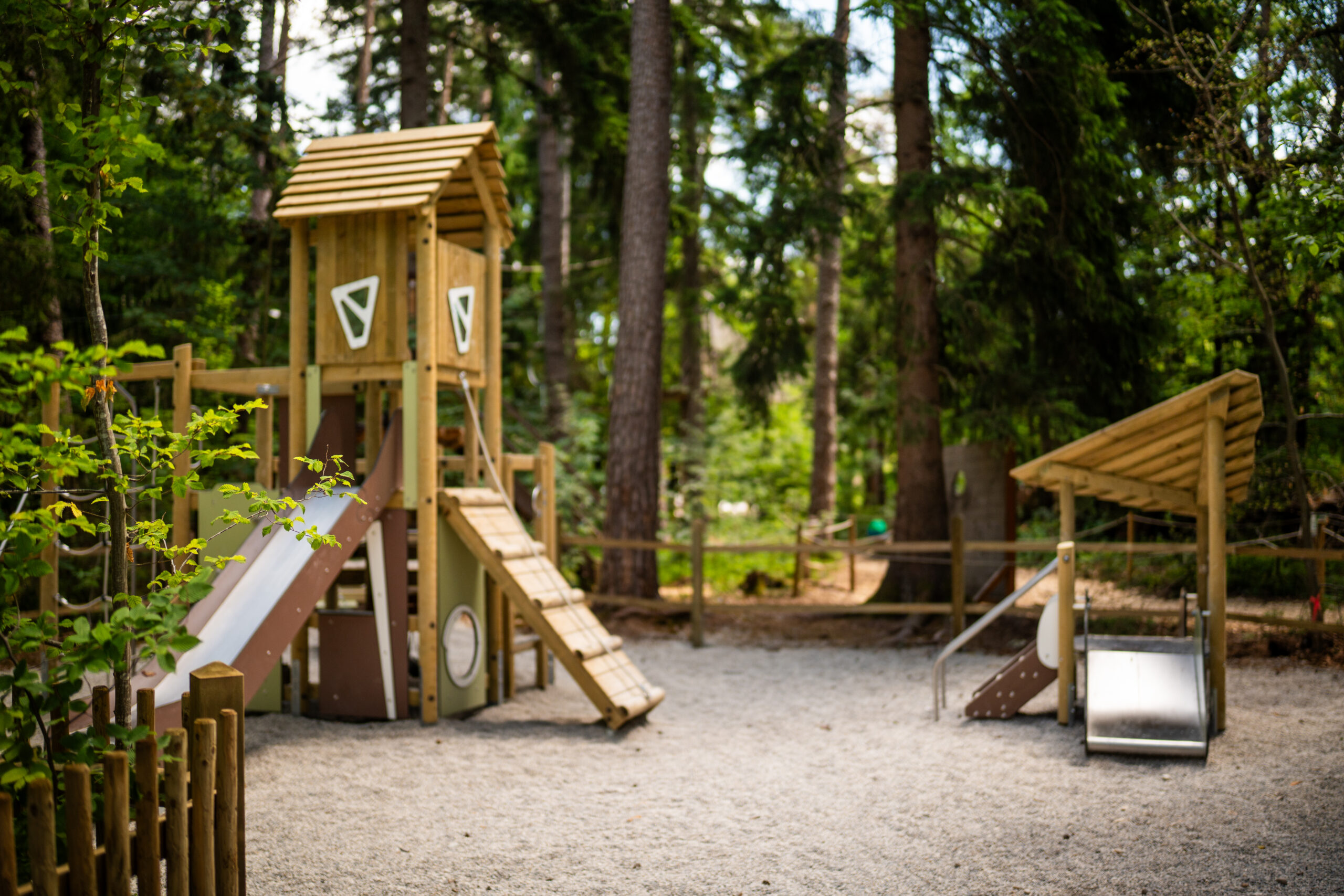 Spielplatz im Münchner Wald mit Rutsche, Klettergerüst und kleiner Bereich für Kinder. Alles mit Sand.