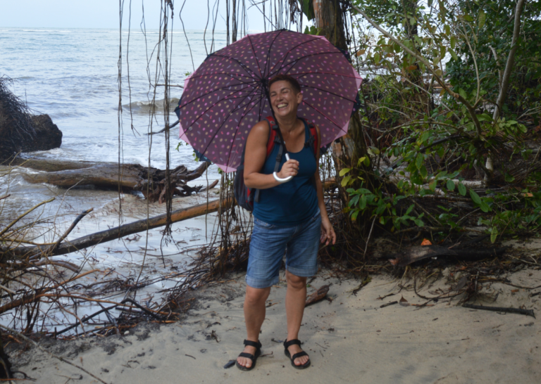Elisabeth Gruber, Grafikerin. Mit Regenschirm am Strand, lachend in die Kamera.